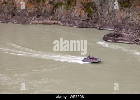 Luftaufnahme von einem grauen Gummi Motorboot segeln auf einem grünen Fluss in den Bergen zwischen Felsen und Klippen Stockfoto