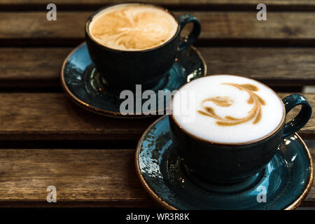 Zwei schöne rosa Tassen Cappuccino mit Latte Art auf dem hölzernen Tisch Stockfoto