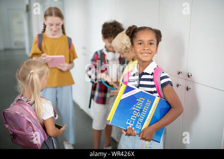 Dunkelhäutige Mädchen mit Englisch Grammatik in der Nähe von Freunden Stockfoto