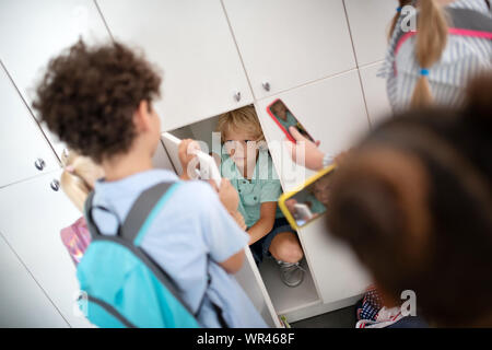 Unhöflich Kinder Mobbing armer Junge in der Umkleide sitzen Stockfoto