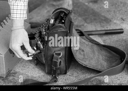 Mans Arm gezeigt Kommissionierung Schrotflinte Patrone aus Ledertasche auf dem Boden (monochrom) Stockfoto