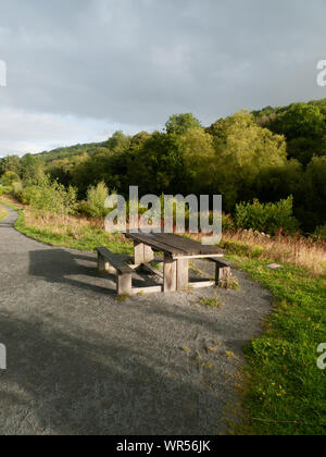 Hölzerne Picknickbank auf einem Fußweg in einem bewaldeten Tal Stockfoto