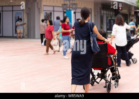 Tochter ihre Mutter im Rollstuhl spazieren Sie entlang der Shopping Mall. Stockfoto