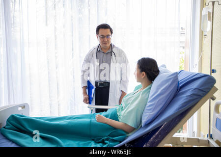 Die Ärzte sind gefragt und erklärt über die Krankheit zu einer Patientin im Bett liegend an einem Krankenhaus. Stockfoto