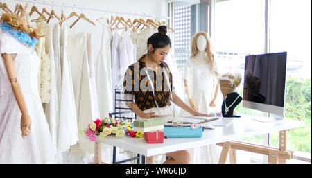 Small Business der asiatischen Frauen Mode Designer arbeiten und die Verwendung von Smartphones und Tablet mit Brautkleider bei Clothing Store Stockfoto