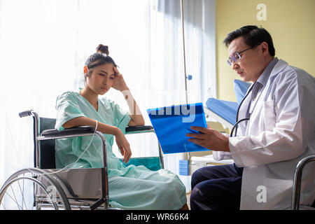Die Ärzte sind gefragt und erklärt über die Krankheit zu einer Patientin im Rollstuhl im Krankenhaus Stockfoto
