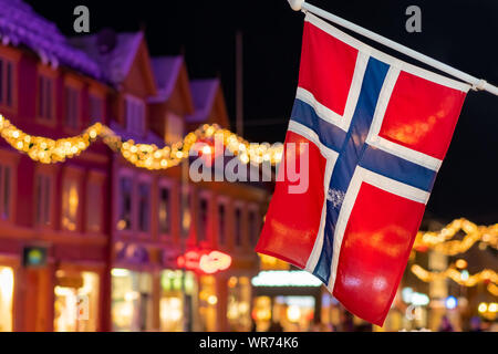 Norwegische Flagge an einem Pol in Tromso Zentrum in der Weihnachtszeit nach Einbruch der Dämmerung, Norwegen Stockfoto