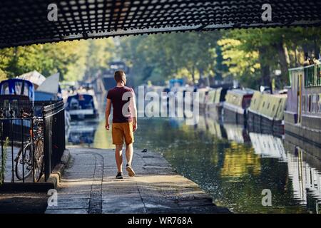 Junger Mann zu Fuß an der Strandpromenade von Regents Canal mit Booten. Little Venice in London, Vereinigtes Königreich. Stockfoto