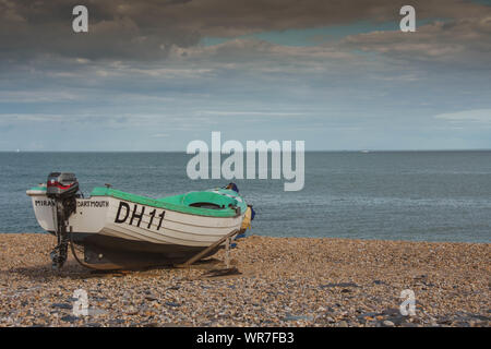 Eine grüne und weiße Fischerboot auf dem Kiesstrand mit Blick auf das Meer und ein bewölkter Himmel Stockfoto