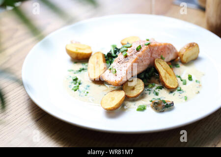 Lachsfilet mit gebackenen Kartoffeln auf einem Sahne mit Schnittlauch Stockfoto