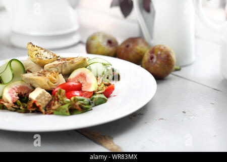 Eine leichte vegetarische Salat mit Feigen, Artischocken, Gurken, Tomaten, Feta auf Rucola Blätter, gekrönt mit Himbeersauce. Stockfoto