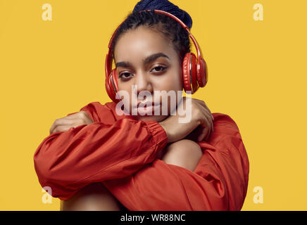 Portrait von wunderschönen afrikanischen brunette teenage Mädchen mit Dreadlocks tragen einen roten windbreaker Musik hören über kabellose Kopfhörer isoliert auf Vivi Stockfoto