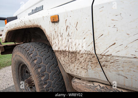 Vorne auf der Beifahrerseite vor einer weißen 4WD Toyota Land Cruiser Troop Carrier (aka Troopie) geparkt und mit Schlamm bespritzt Stockfoto