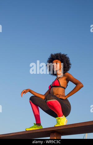 Glückliche junge afrikanische Frau dehnen und Aufwärmen vor einem Outdoor Training. mit einem schönen blauen Himmel Hintergrund Stockfoto