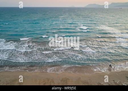 Weiß schäumende Wellen im Meer, Schwimmen und Laufen die Leute auf der Sandstrand auf der Vorder- und nebligen Hochland am Horizont in den Abend. Abend sur Stockfoto
