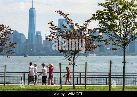 New Yorker Familie, Blick auf eine Familiengruppe, die auf Liberty Island mit der Skyline von Lower Manhattan in der Ferne spazieren geht, New York City, USA. Stockfoto