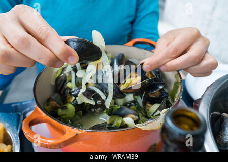 Horizontale Ansicht der Hände einer Frau essen traditionelle Muscheln und Pommes frites Gericht namens 'Moules et Frites' Stockfoto
