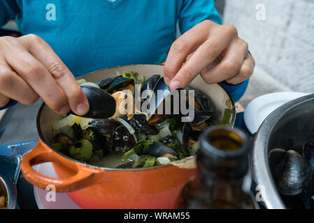 Horizontale Ansicht der Hände einer Frau essen traditionelle Muscheln und Pommes frites Gericht namens 'Moules et Frites' Stockfoto