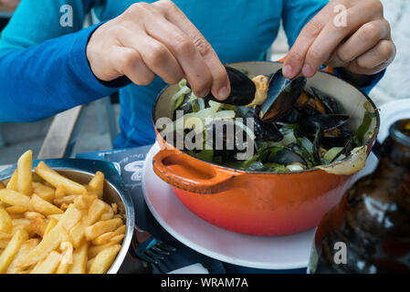 Horizontale Ansicht der Hände einer Frau essen traditionelle Muscheln und Pommes frites Gericht namens 'Moules et Frites' Stockfoto