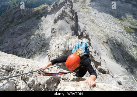 Horizontale Ansicht einer attraktiven Blondine weiblichen Kletterer auf einem steilen Klettersteig in den italienischen Dolomiten mit tollem Blick hinter Stockfoto