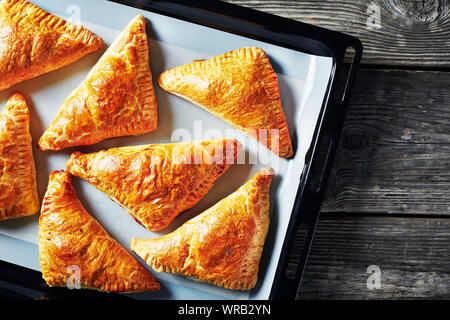Frisch gebackenen Blätterteig apple Umsatz auf ein Blatt pan auf einem alten Holztisch, Ansicht von oben, flatlay, close-up Stockfoto