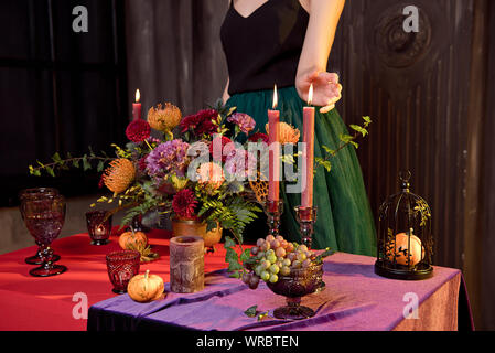 Die Frau Hände bereiten Dekorationen für Halloween Tisch mit Kerzen ein Kupfer Vase mit Blumen Stockfoto