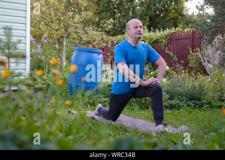 Senior hsipanic Mann ist Arbeiten in Garten, stehen in 1 oder Virabhadrasana Krieger darstellen. Yoga für Gesundheit im Alter. Stockfoto