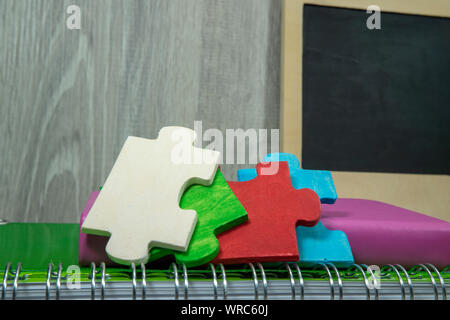 Zurück zum Konzept der Schule mit bunten Holz Puzzleteile, Bücher und Chalk Board auf dem Tisch gegen eine graue Wand mit freiem Speicherplatz kopieren Stockfoto
