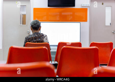 Alte Frau auf orange Stuhl warten auf das Gesundheitswesen im Krankenhaus sitzen. Stockfoto