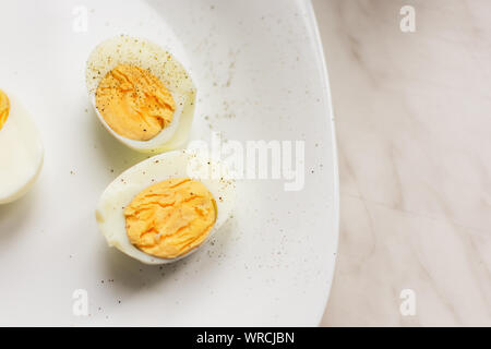 Die beiden Hälften des hart gekochte Eier auf weißer Keramik platte Ansicht von oben. Ernährung Konzept. Stockfoto