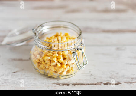 Dose Mais in Glas Glas auf hölzernen Tisch Hintergrund. Stockfoto