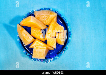 Mehrere Stücke von Orange muskmelon auf blauem Hintergrund, Obst Stücke sind in eine blaue Schale Stockfoto