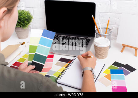 Frau Schreiben von Zahlen der Farben im Notebook auf Office Tabelle mit Laptop und Tasse Kaffee Stockfoto
