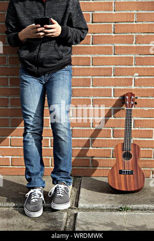 Junge ukulele Player auf Pause Kontrolle des Smartphones Stockfoto