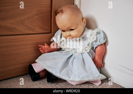 Alt, abgenutzt und schmutzig Spielzeug Puppe mit einem unheimlichen Blick, der in der Ecke des Raumes sitzt. Stockfoto