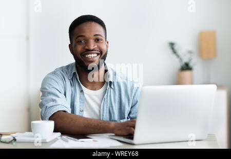 Afrikanische Arbeiter mit Laptop, lächelnd und trinken Kaffee im Büro Stockfoto