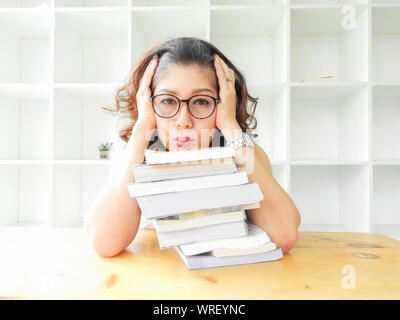 Schöne Frauen in Gläsern auf dem Tisch durch eine Menge Bücher zerdrückt, sehr betont der Studie. Stockfoto