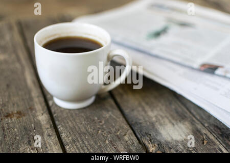 Weiße Tasse Kaffee und Zeitung auf alten, hölzernen Tisch. Selektive konzentrieren. Stockfoto