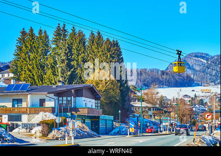 St. Gilgen, Österreich - Februar 23, 2019: Der alte gelbe Gondel der Seilbahn Zwolferhorn Fahrten über die Straße des Dorfes, am 23. Februar in St. Gilg Stockfoto