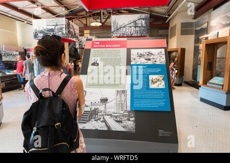 Konzept des Frauenmuseums, Rückansicht einer jungen Frau mit Rucksack und Blick auf eine Ausstellung im Ellis Island Museum, New York City, USA.