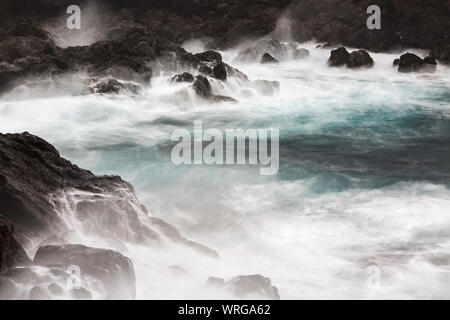 Lange Belichtung geschossen von Tall plätschernden Wellen schlagen die Felsen mit kleinen Wasserfällen, am Playa de Nogales in La Palma, Spanien. Stockfoto