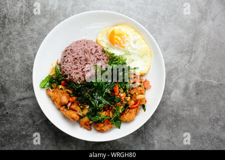 Knusprige Hähnchen mit grünem Basilikum zubereitet, serviert mit gedämpftem Reis und Spiegelei, warmen und würzigen Gericht mit Basilikum. Stockfoto