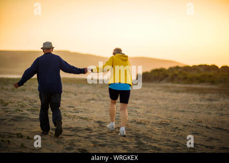 Ältere Paare genießen Sie spazieren gehen zusammen am Strand bei Sonnenuntergang. Stockfoto