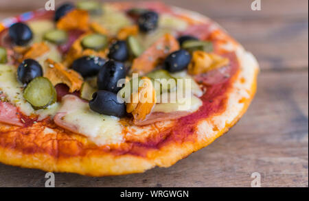 Hausgemachte Pizza mit Tomatensauce, Käse, Oliven, Schinken und Pilzen auf Holztisch. Selektiver Fokus Stockfoto