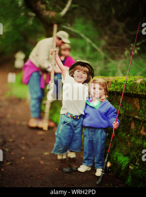 Vorderansicht von zwei kleinen Kindern für die Kamera posieren auf einem Bemoosten Brücke. Stockfoto