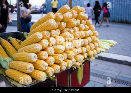 Bank Verkauf von gekochten Mais. Gekochten Mais und heißes Wasser im Kessel. Ungekocht raw Hühneraugen vor der Arbeitsplatte. Stockfoto