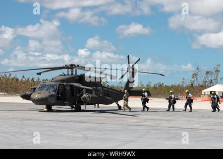 Ein Soldat der US-Armee Escorts von der US-Behörde für Internationale Entwicklung Personal und Mitglieder des Böhmischen Polizei gegen eine U.S. Army UH-60 Hubschrauber zu Such- und Rettungsmaßnahmen im Rahmen des Hurrikans Dorian Relief in Marsh Harbour Airport, Marsh Harbour, Abaco Islands, Bahamas, Sept. 9, 2019 durchführen. Zur Unterstützung der Außenpolitik der USAID Katastrophenhilfe, DOD ist einzigartige militärische Fähigkeiten die umfassendere Reaktion zu ermöglichen. Die Verteidigungsminister autorisierten US Northern Command Transport Logistik für die Bewegung von USAID und Dritten humanitar zur Verfügung zu stellen Stockfoto