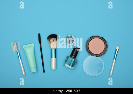 Feminine Beauty Care Flach von face makeup Blush, Bürsten, Nagellack und Glitter auf blauem Hintergrund, erhöhte Ansicht von oben, direkt über Stockfoto