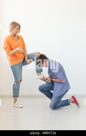 Junger Mann kniet und ehrfürchtig Schnürsenkel binden an Seine herrschsüchtige nicht identifizierte Frau auf einem weißen Hintergrund posiert. Konzept der beherrschenden Beziehungen Stockfoto