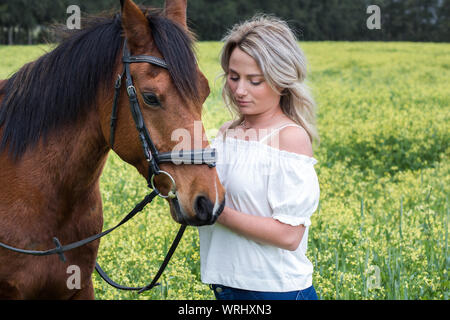 Nahaufnahme einer Frau die Interaktion mit Ihrem Kastanie arabischen Pferd draußen mit der gelben Blüten. Stockfoto